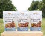 Three bags of Goodson Pecans on a wooden block with a green outdoor background