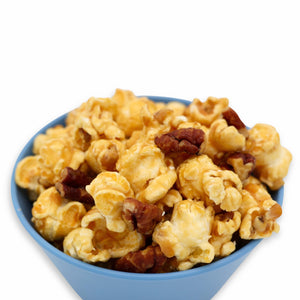 A blue bowl filled with caramel coated popcorn and pecans against a white background.