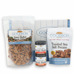 A package of Goodson Pecans Fancy Shelled Pecan Halves, a small jar of Goodson Pecans Crunchy Pecan Butter with a small jar of Goodson Pecans Creamy Pecan Butter stacked on top, a package of Goodson Pecans Toasted Sea Salt Pecans, and a Goodson Pecans box against a white background.