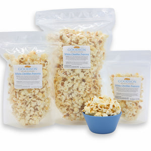 Goodson White Cheddar Popcorn in clear packaging of varying sizes with a small blue bowl of popcorn.