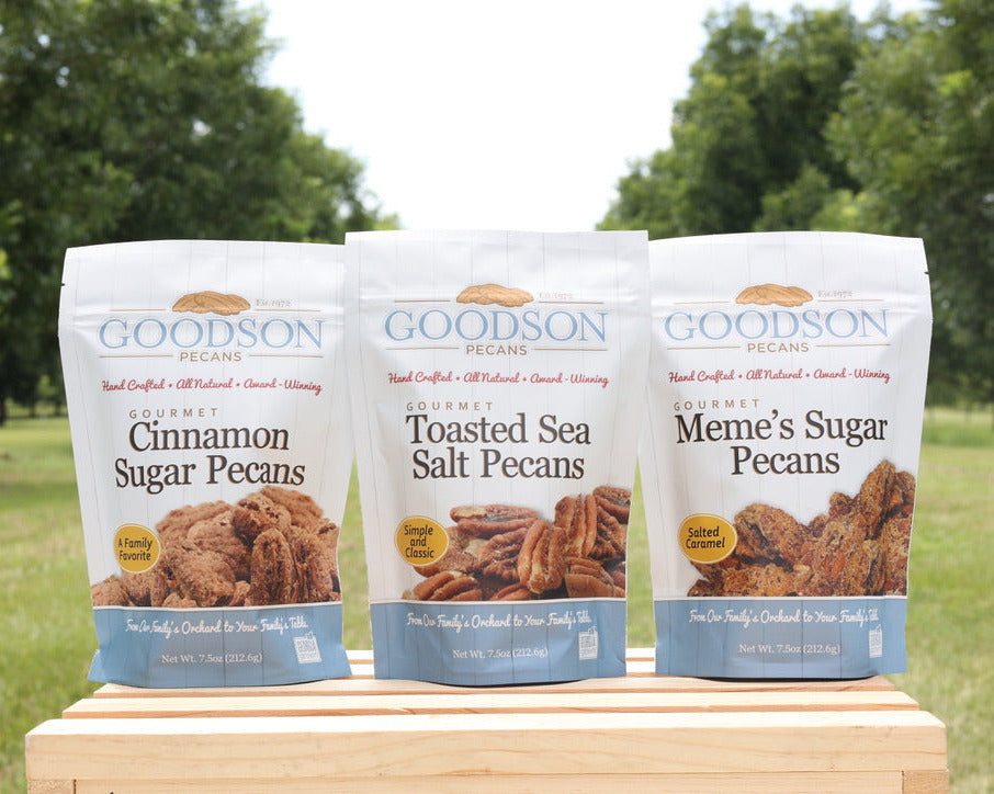 Three bags of Goodson Pecans on a wooden block with a green outdoor background