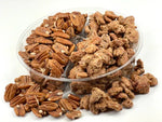 Assorted roasted pecans in a clear plastic container on a white background.