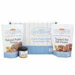 Two packages of Goodson Pecans Natural Praline Pecans, and Toasted Sea Salt Pecans, a small jar of Goodson Pecans Pecan Butter, and a Goodson Pecans box against a white background.