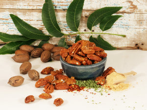Shelled Pecans with a spicy ranch coating in a blue bowl, surrounded by unshelled pecans, shelled pecans with the spicy ranch coating, and various seasonings against a wooden background.