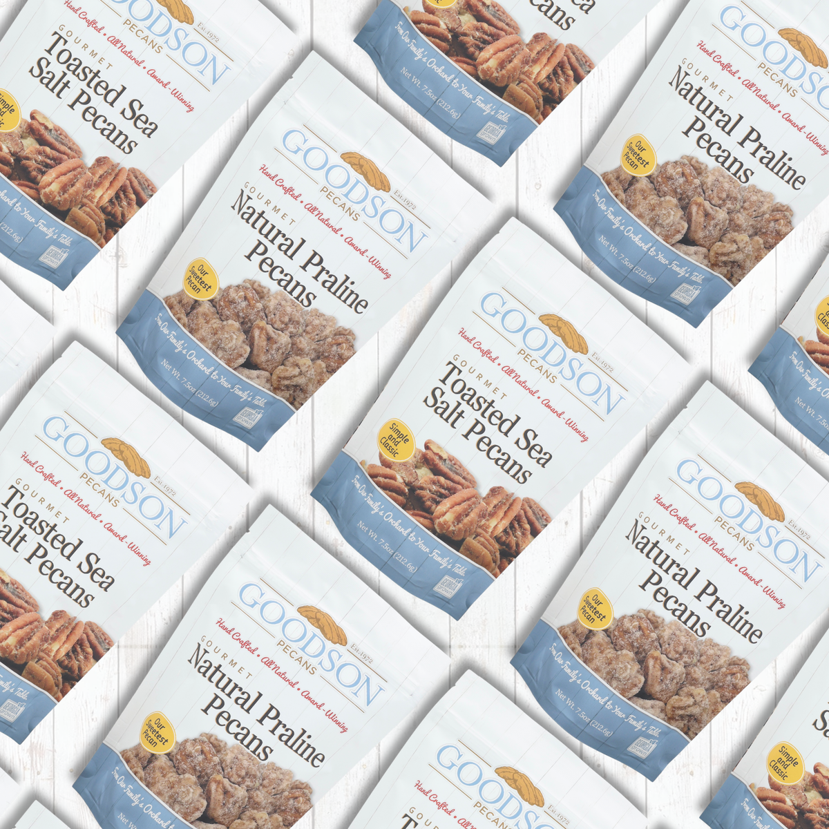 Multiple bags of Goodson Natural Praline Pecans arranged in a repeating diagonal pattern on a white background. The bags are white with blue bands, featuring a photo of toasted sea salt pecans and a yellow circular badge.